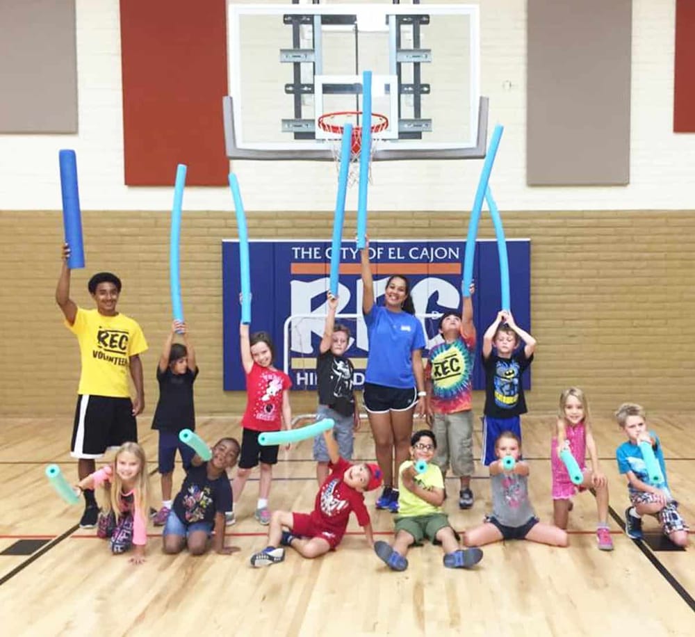 Children's indoor sports activity using pool noodles for fun and exercise at a gym.