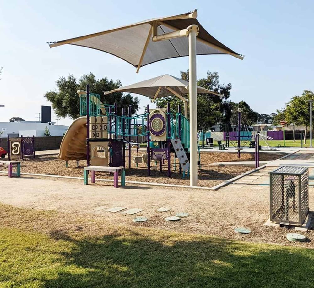 Colorful playground with shade umbrellas in a community park, ideal for family outdoor activities and children's play.