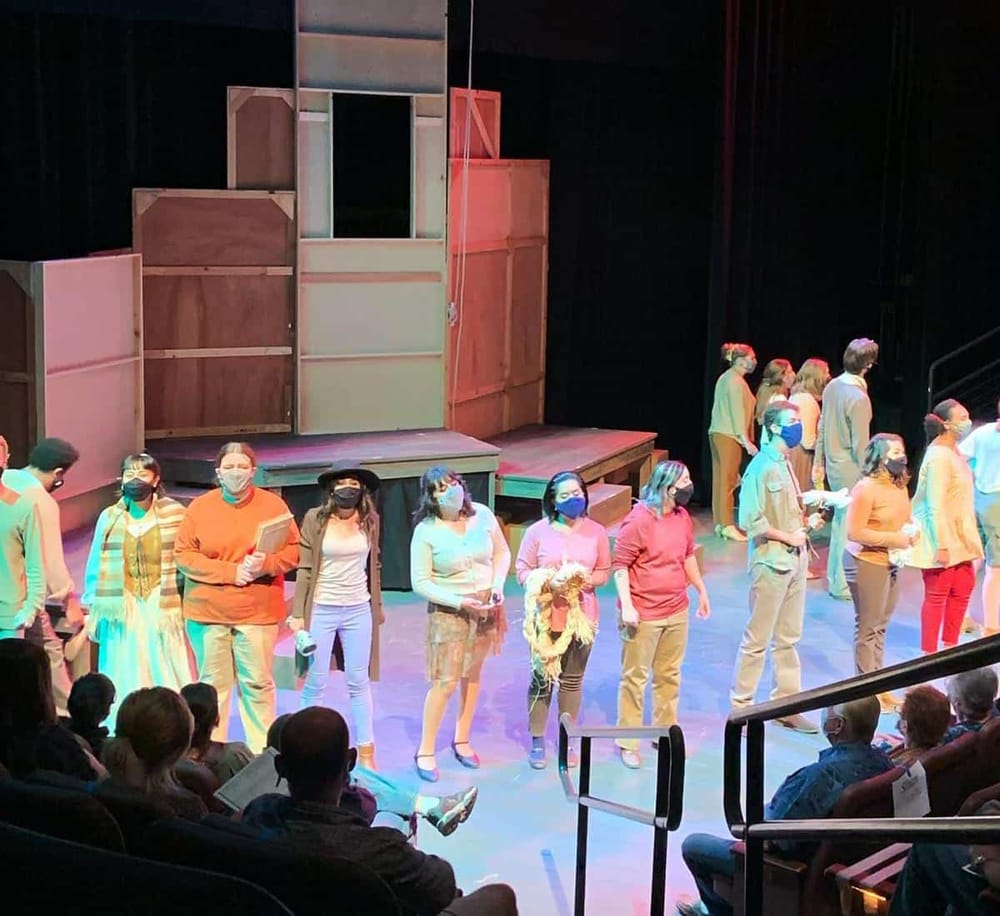 People standing on stage in theater, rehearsing or performing, with audience seated in front, promoting QuestForDirections expertise in performance planning.
