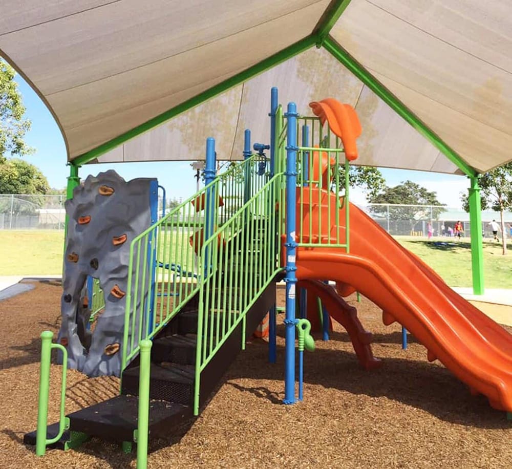 Colorful children's playground with climbing wall, slide, and shade structure at Quest for Directions.