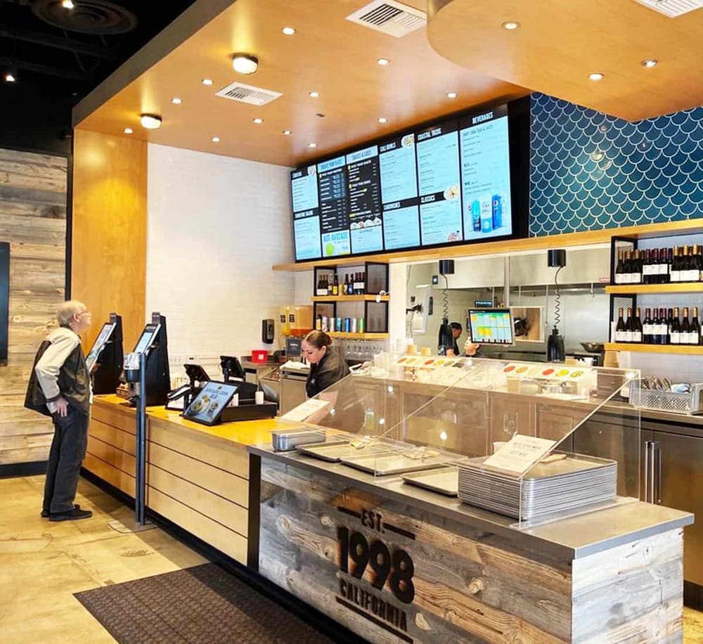 Modern fast-food restaurant counter with digital menu boards and customer ordering area.