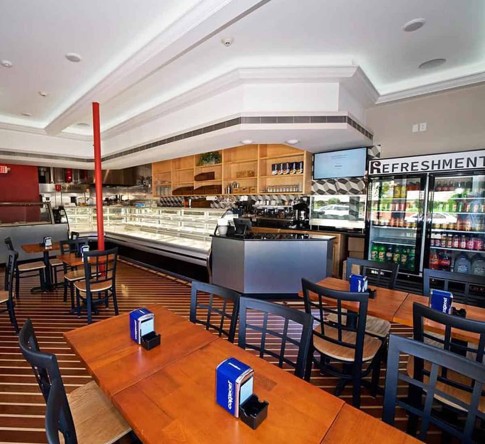 Spacious cafe interior with wooden tables, chairs, beverage refrigeration, and a counter with snacks.