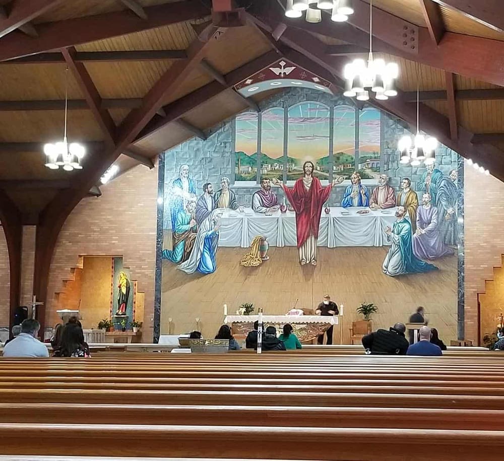 Bright church interior with mural of Jesus Christ at the Last Supper, wooden ceiling, and modern lighting.