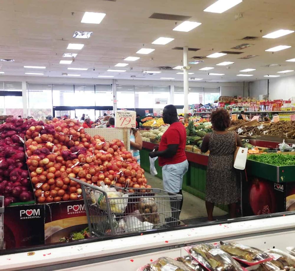 Brightly lit grocery store produce section with fresh vegetables and shoppers shopping for fresh onions.