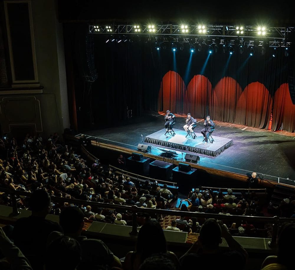 Live music performance on stage with three singers and vibrant stage lighting at a concert venue.