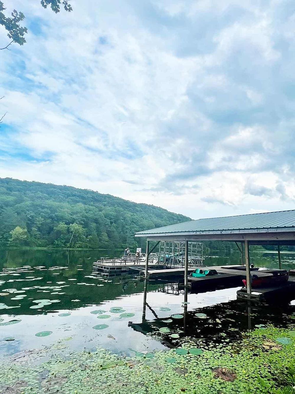 Serene lake with boat dock, lush green hills, and cloudy sky, ideal for outdoor activities and nature exploration.