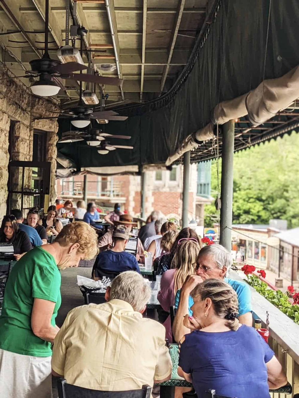 Outdoor dining at a bustling restaurant patio with diverse group of people enjoying meals and conversations.