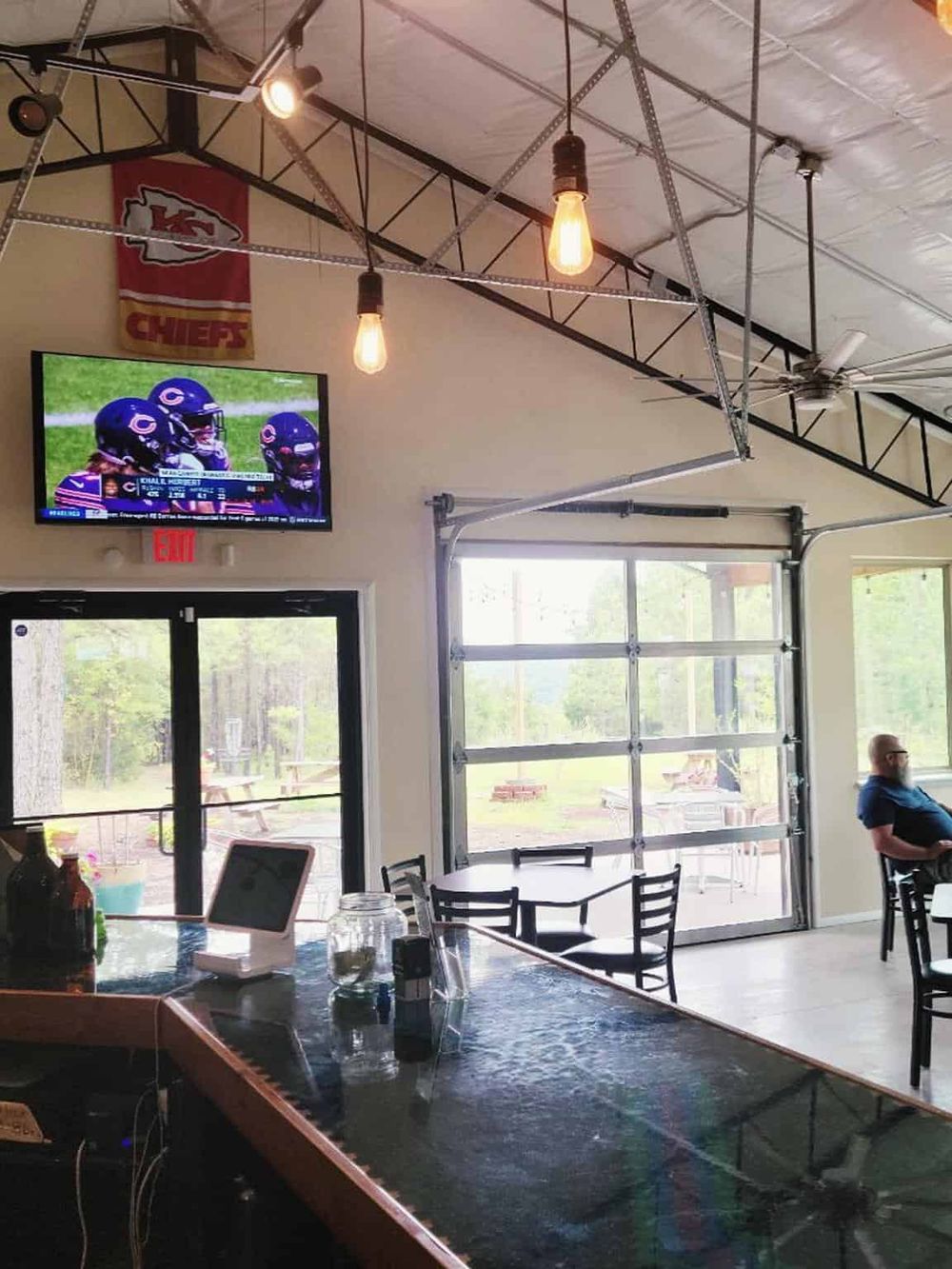 Cozy indoor sports bar with large TV displaying football game, modern industrial decor, and outdoor view.