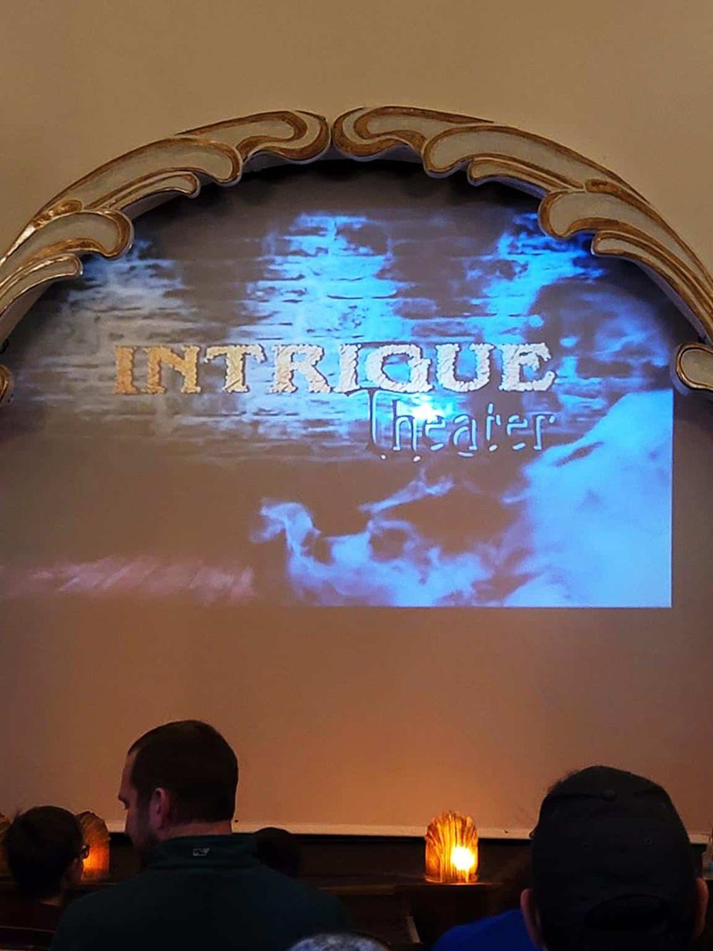 Elegant theater entrance with "Intrigue Theater" projection on stage screen, creating a mysterious ambiance.