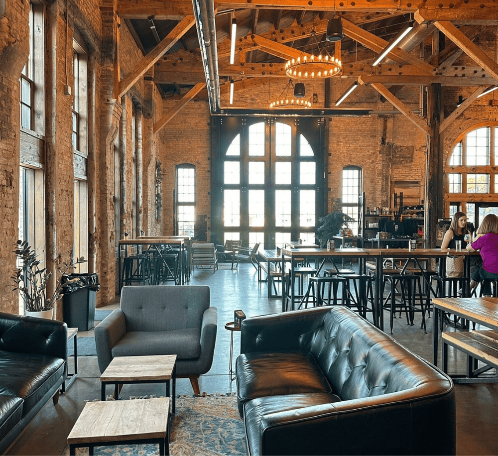 Bright industrial loft interior with exposed brick walls and large windows, perfect event space and community hub.