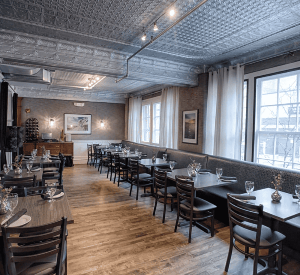 Cozy modern restaurant interior with large windows, wooden floors, and elegant table settings for diners.