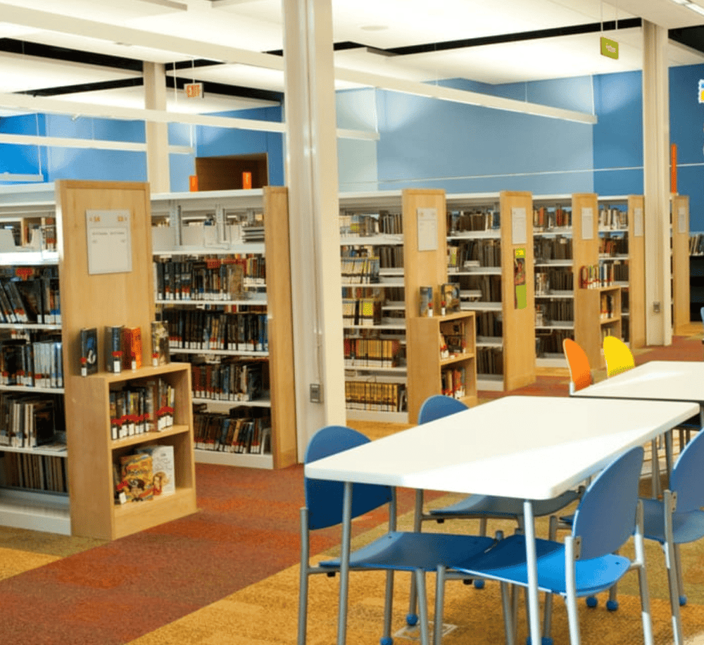 Bright library interior with bookshelves, reading tables, and colorful chairs for students and visitors.