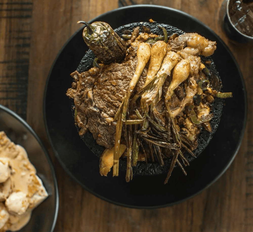 Succulent grilled beef served with roasted green onions and herbs on a black plate.