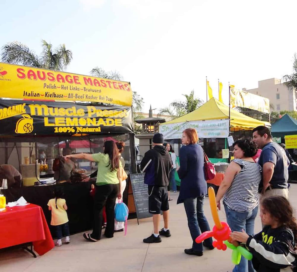 Vegan sausage stand at outdoor food festival with people in line.