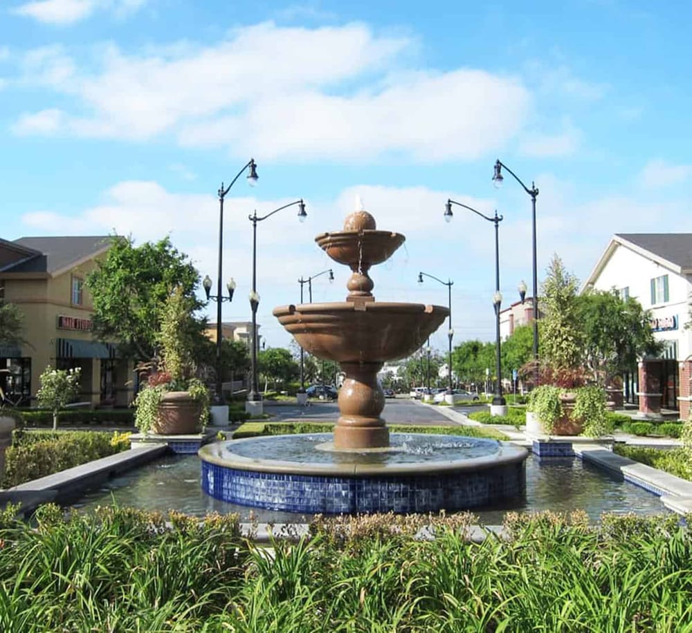 Charming downtown shopping center with fountain, trees, and colorful storefronts, perfect for local shopping and dining.