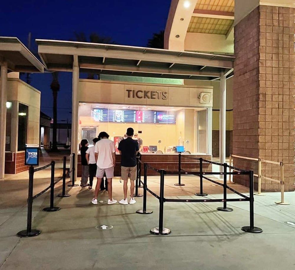 People buying movie tickets at cinema ticket counter in the evening, queueing at ticket sales booth.