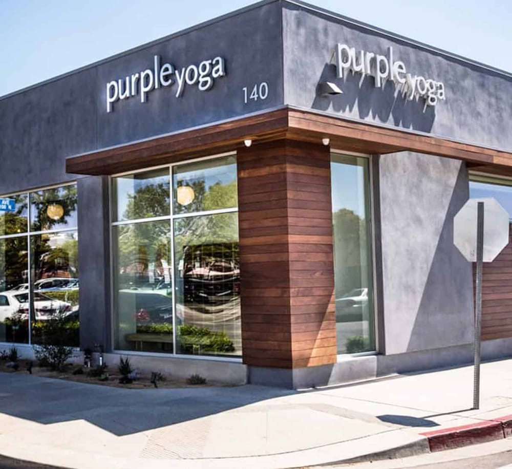 Modern yoga studio exterior with "Purple Yoga" signage, large glass windows, and stylish wooden accents.