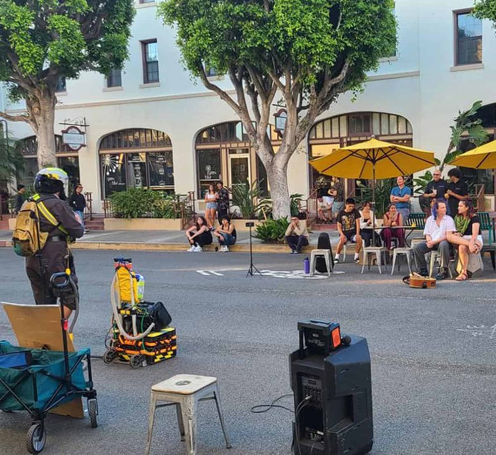 Stunt performer with fire safety equipment prepares for street performance in lively outdoor cafe area.