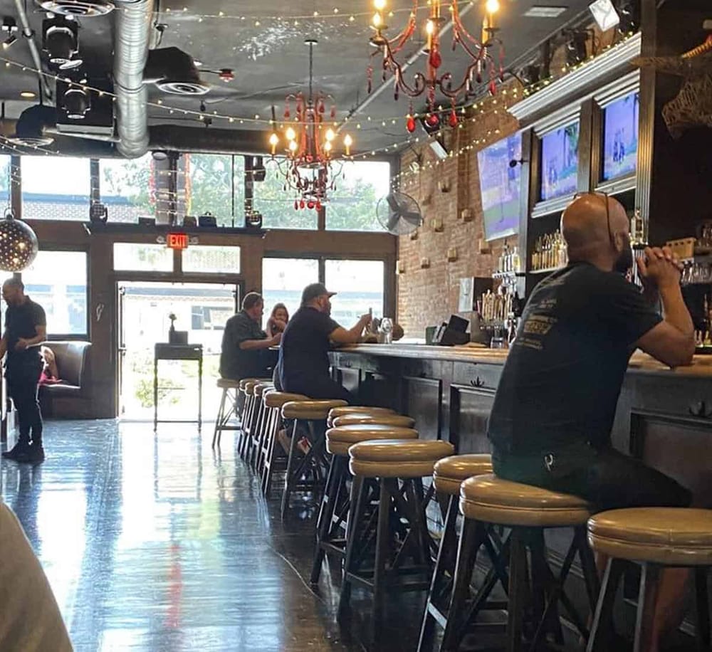 Cozy bar interior with televisions, string lights, and seating near the window.