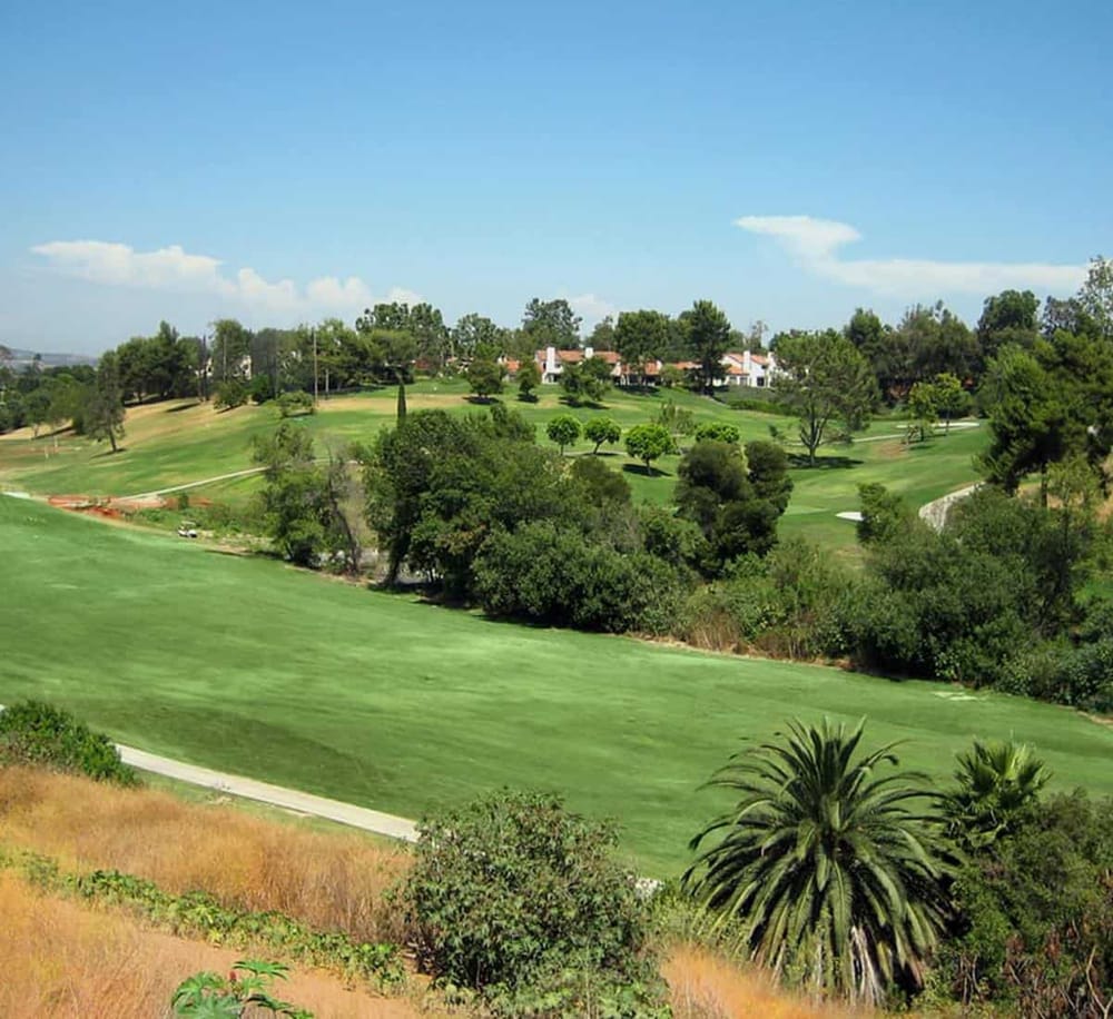 Golf course with lush green fairways and trees, scenic landscape, and residential area in the background.