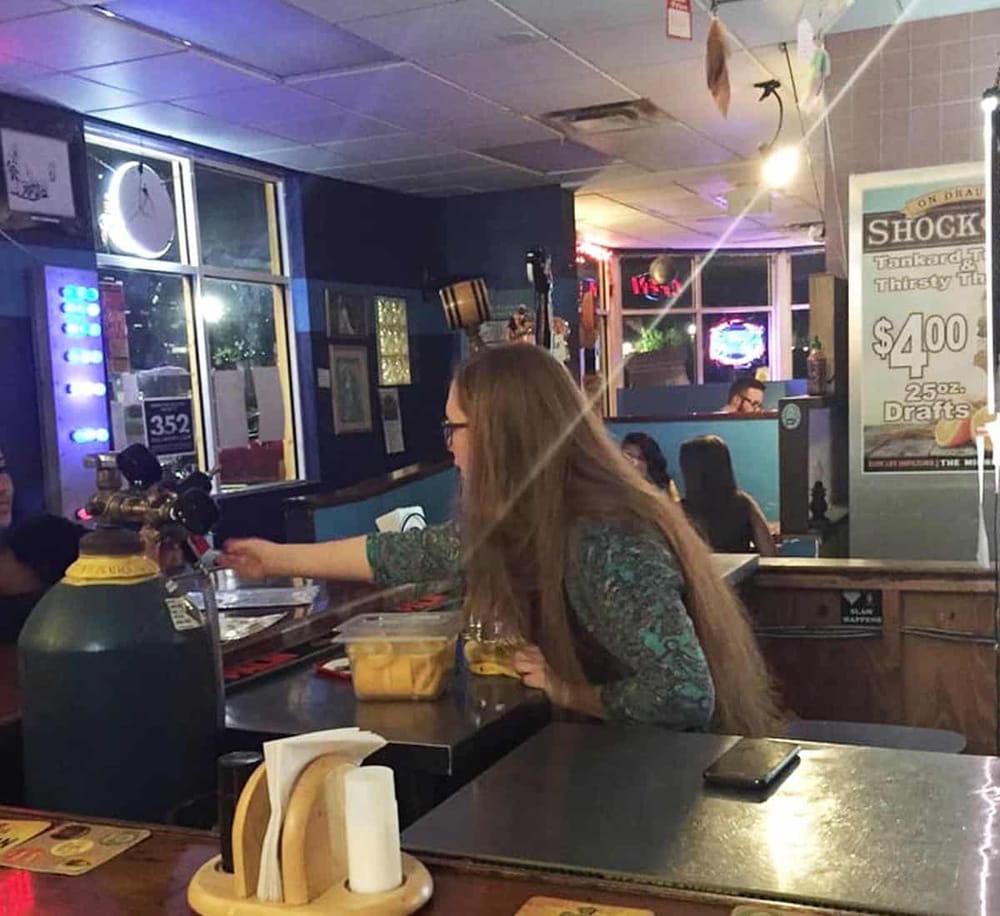 - Female bartender serving drinks at a bar in a lively nightclub or restaurant setting.