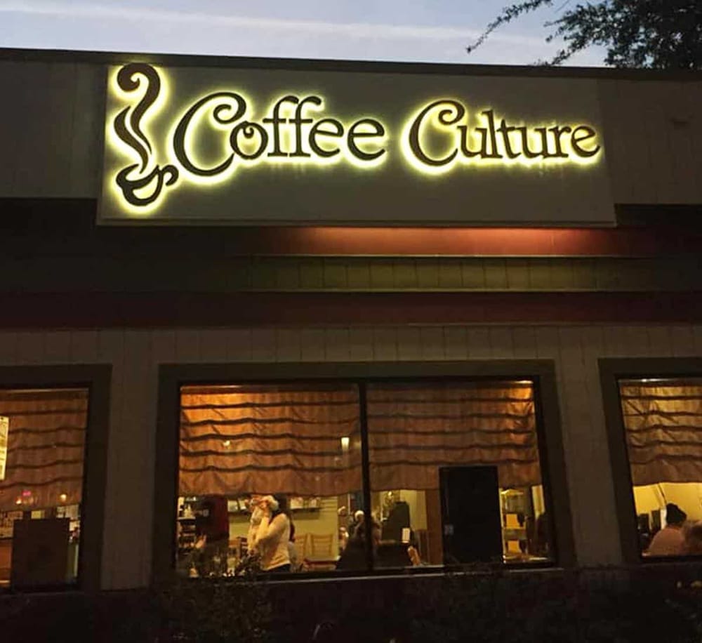 Coffee Culture neon sign illuminated at dusk in a cozy café setting.