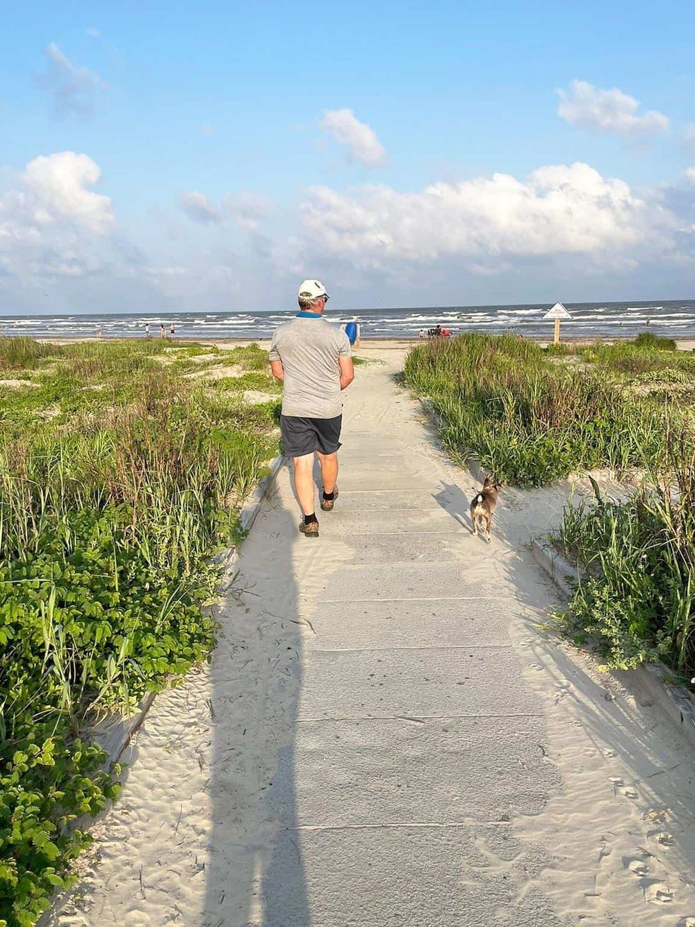 Beach boardwalk leading to the ocean with a man and dog enjoying the seaside, perfect for beach vacation destination SEO.