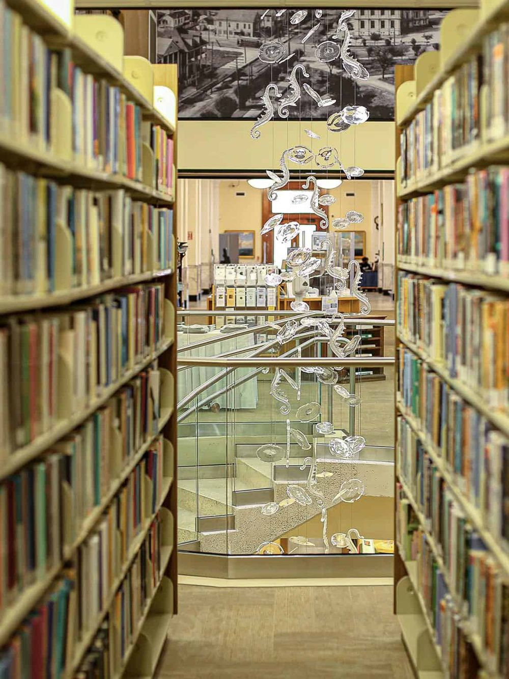 Colorful library shelves with abstract hanging art and a staircase in the background, showcasing a modern and inviting library space.