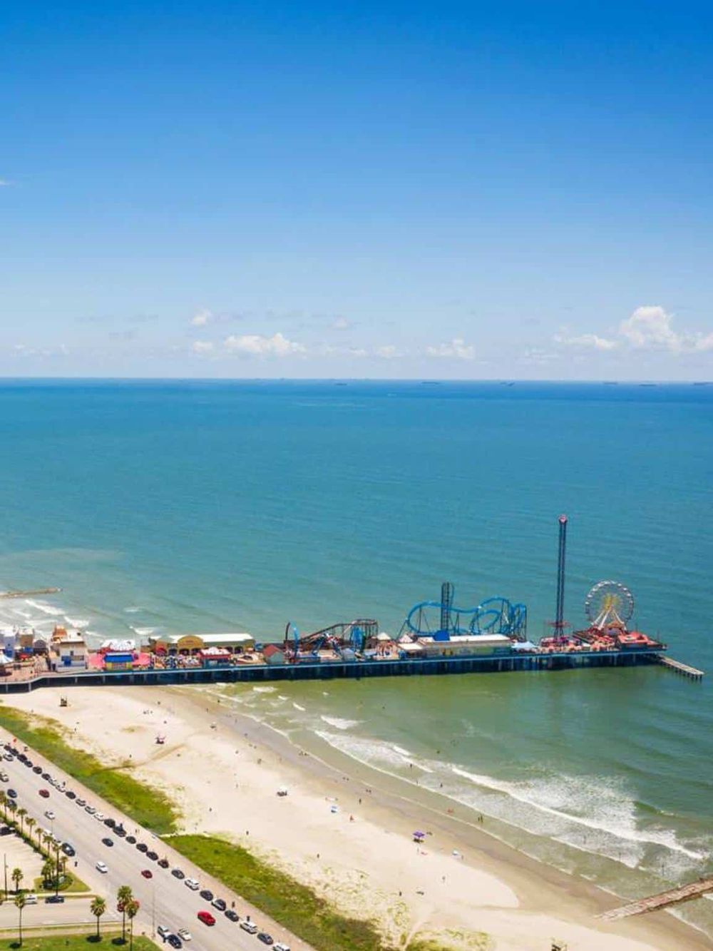 Vivid aerial view of a beachside amusement park with roller coasters and Ferris wheel by the ocean.
