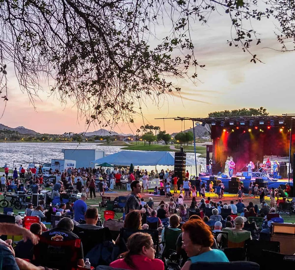 Vibrant outdoor concert at sunset by the water with a large crowd and stage performance, ideal for exploring event planning and entertainment venues.