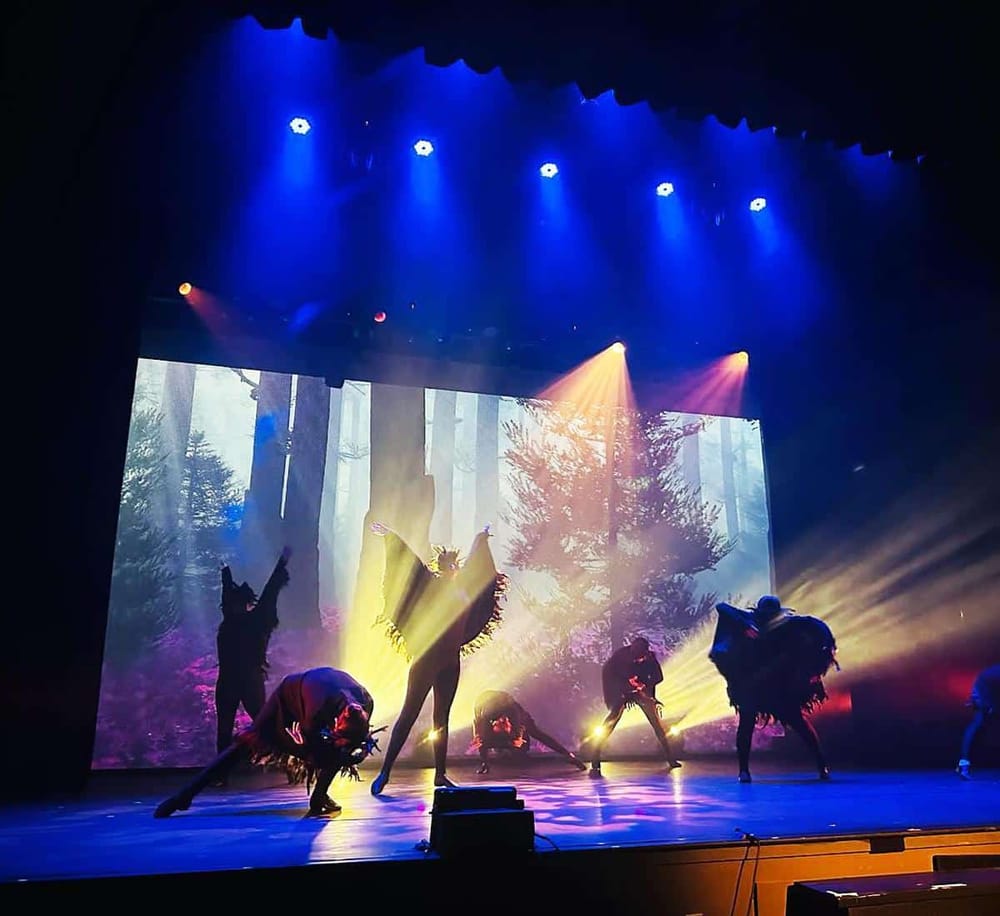 Bright stage lighting illuminates performers during a theatrical dance showing.