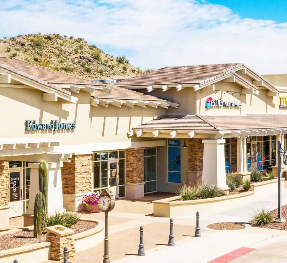 Modern shopping center storefront with Leslie's and Edward Jones signage, desert landscape, and mountain background.