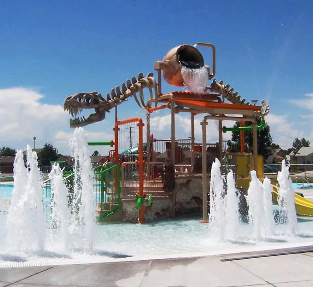 Colorful water playground with dinosaur-themed splash pad and fountains for kids' outdoor fun.