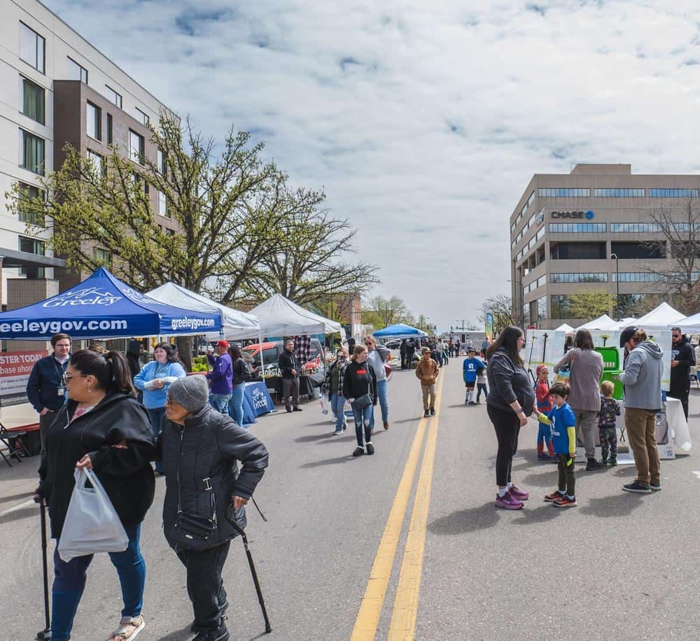 Accessible community event outdoor street fair with local booths, families, and cityscape background.