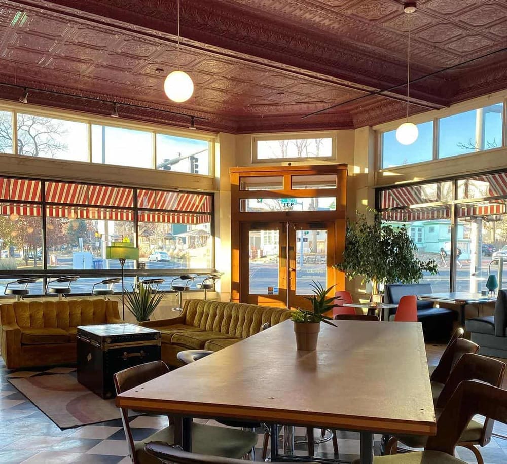 Cozy coffee shop interior with large windows, vintage decor, and comfortable seating area.