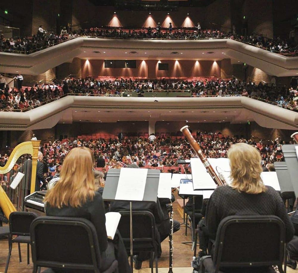 Aerial view of symphony orchestra performing in a large concert hall filled with audience.
