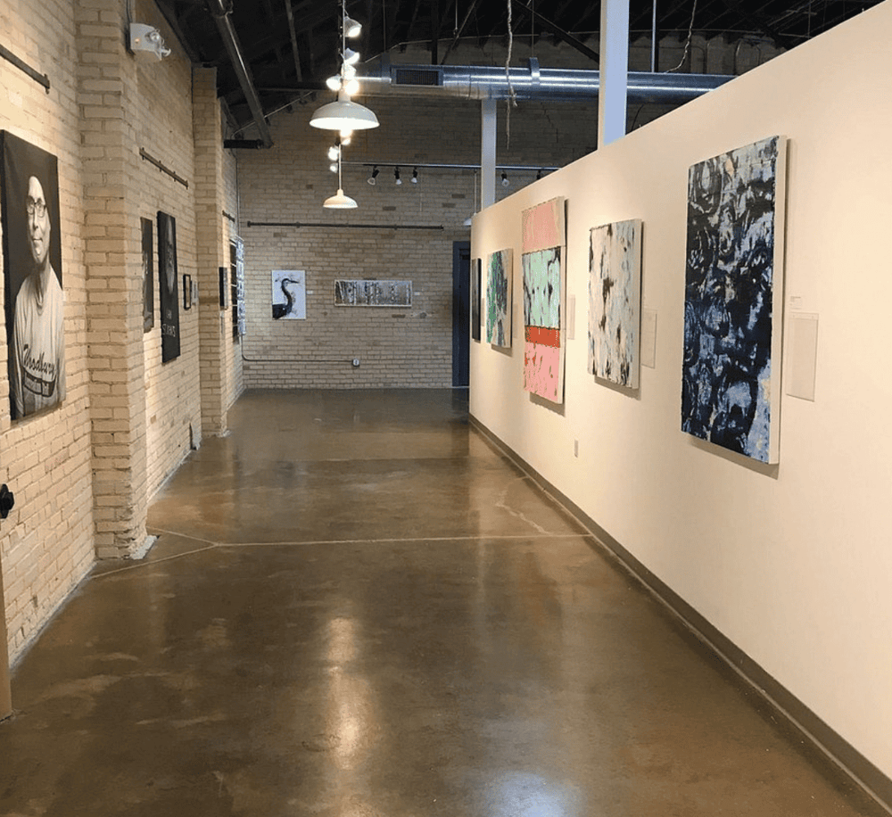 Contemporary art gallery featuring colorful abstract and portrait paintings in an industrial-style space.