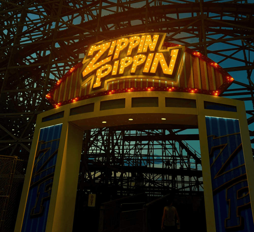 Zoomed-in view of the vibrant "Zippin Pippin" wooden roller coaster entrance at dusk, highlighting amusement park thrill rides.