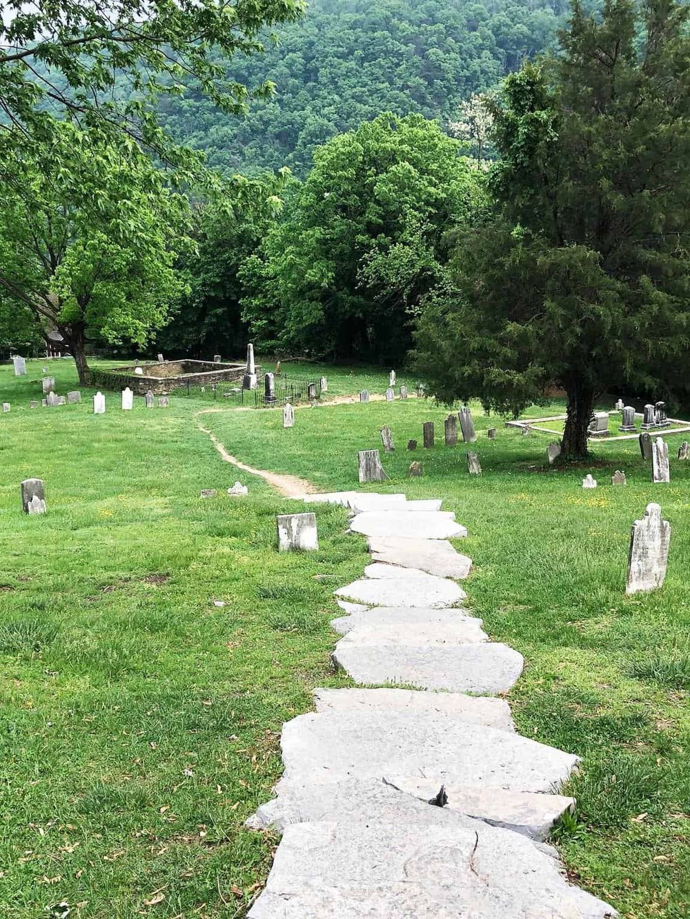 Peaceful cemetery with stone pathway and lush green trees, scenic mountain backdrop, ideal for reflection and outdoor scenery.