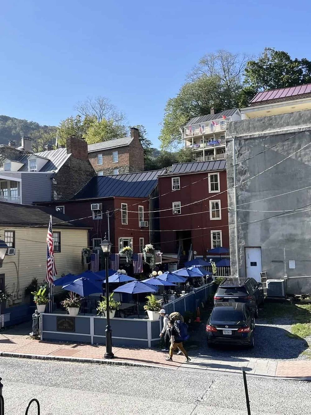 Charming outdoor restaurant with blue umbrellas and historic brick buildings in a hilly, scenic town.