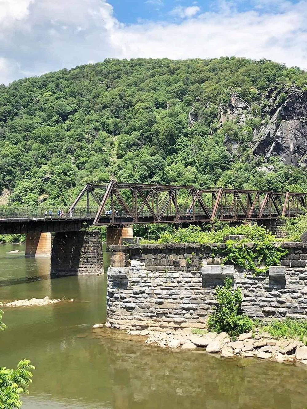 Historic bridge over river in lush green mountains with clear sky.