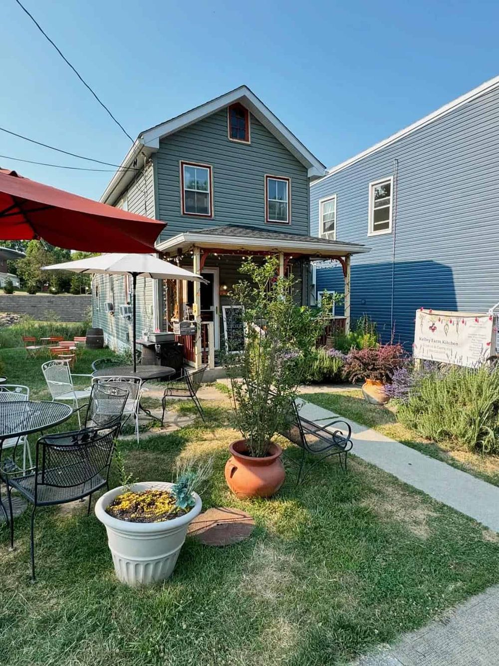 Charming outdoor cafe seating area with colorful umbrellas, potted plants, and garden decor in front of a vintage house.