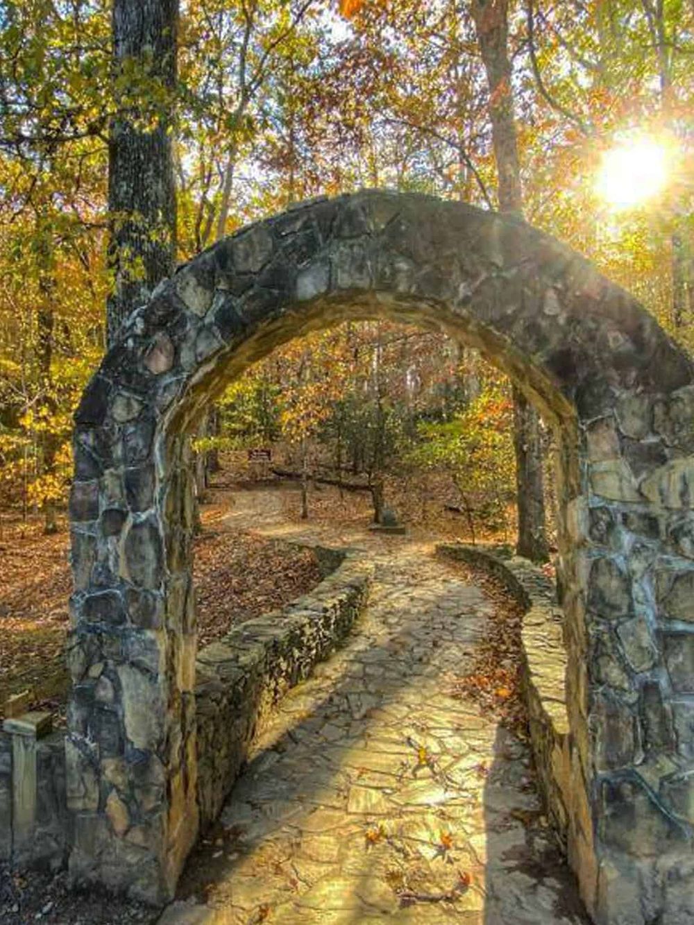 Old stone archway in a sunlit autumn forest, scenic nature trail.