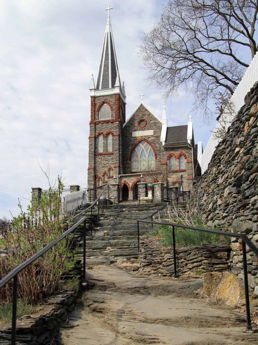 Historic church on a hill, accessible via stone steps, surrounded by trees and stone walls, perfect for spiritual travel and architecture tours.