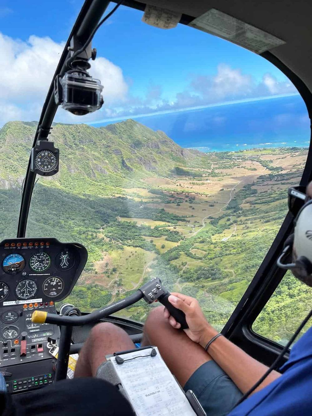 Aerial view helicopter cockpit overlooking lush green mountains and ocean scenery.