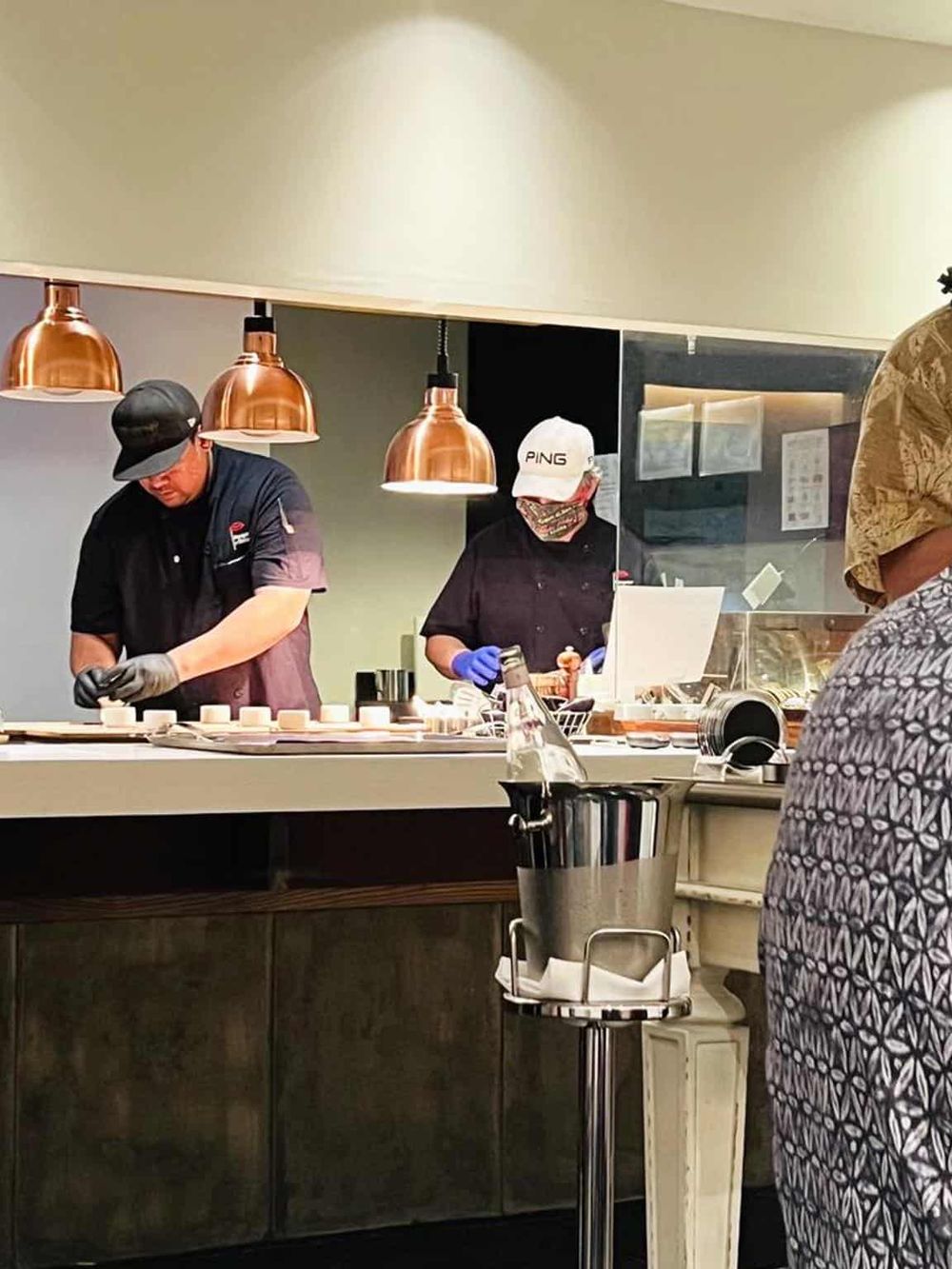 Chefs preparing dishes at a modern restaurant kitchen with copper pendant lights.