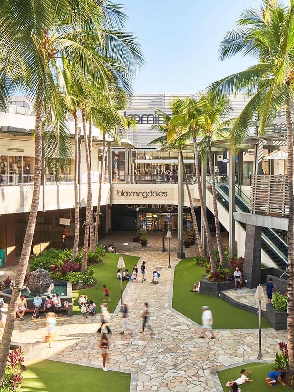 Outdoor shopping mall surrounded by palm trees and walkways, featuring Bloomingdale's department store.