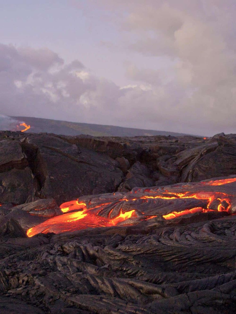 Flowing lava in volcanic landscape at dusk, erupting lava rivers in Hawaii.