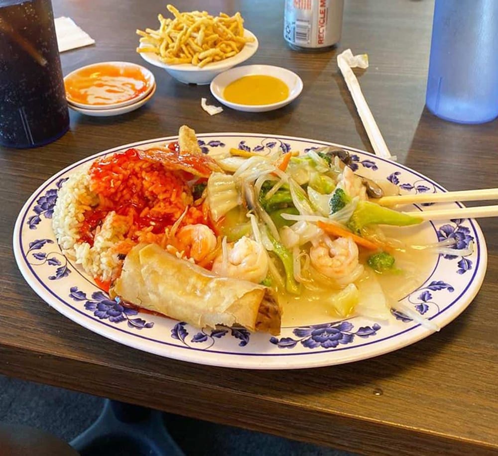 Fresh Asian seafood dish with rice, spring roll, vegetables, and sauces at a restaurant.