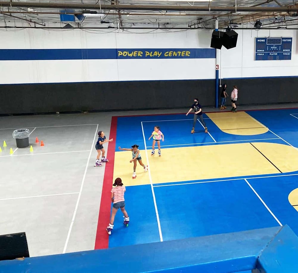 Kids roller skating in indoor sports center with basketball court.